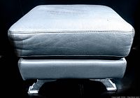 Side view showing light grey leather upholstery and polished stainless steel curved legs.