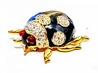 Front angled view of the ladybug brooch showing black enamel body, gold-tone legs and red enamel eyes with rhinestone spots.