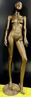 Full assembled vintage fiberglass female mannequin in bronze color standing on round base.