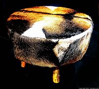 Side view of round footstool showing cowhide upholstery and wooden legs with natural colors.