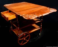 Side angled view of the solid wood tea cart showing carved top surface, pull-out drawer, and wheels