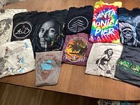 Top down image showing all eleven graphic T-shirts laid out, featuring distinct graphic designs including Bob Marley and tie-dye Santa Monica Pier.