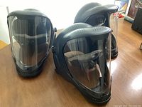 Front view of three black paintball helmets with clear face shields arranged on table