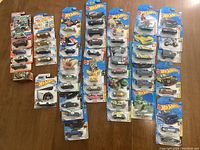 Overhead photo showing multiple rows of packaged Hot Wheels and Matchbox vehicles arranged side by side on a wooden surface.