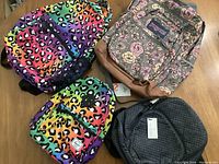 Four backpacks laid flat on a wooden surface showing front and top views with different patterns.