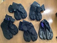 Five pairs of black ninja tabi shoes; four identical pairs with Velcro straps and one differing pair with purple lining.