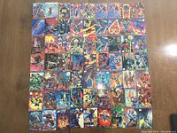 Top-down view of a 63-card assortment of Marvel trading cards arranged in a grid on a wooden surface showing various superheroes and super-villains in colorful artwork.