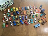 View showing 52 toy cars, mostly Hot Wheels, arranged in rows on a wooden table with various colors and designs, highlighting diversity of vehicles including some Disney Pixar Cars.