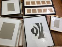 14 assorted picture frames in different sizes and finishes stacked on a floor showing front and back with empty mats.