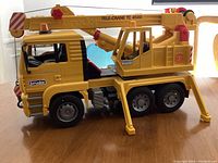 Side view of yellow Bruder Tele-Crane TC 4500 toy crane truck with detailed cabin, six wheels, and extended stabilizing legs