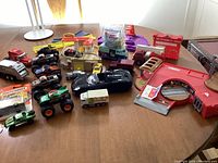 Wide display of toy collection including McDonald's drive thru play set, various monster trucks, die-cast cars, and Tonka Happy Meal toy on table.