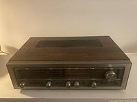 Front angle view of Luxman AM/FM stereo tuner amplifier showing wooden top and metal front panel with knobs and tuning dial.