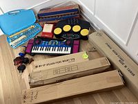Overview of all musical instruments and hardware included in the lot showing the keyboard, drum machine, xylophone, and accessory boxes for stands.