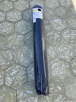 Rolled black round shaggy rug still in original plastic packaging on ground.