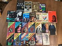 Top view of various paperback books spread on a surface showing front covers of 22 books.