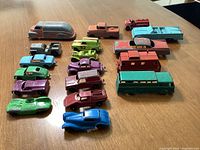 Top-down view of all 18 vintage diecast toy vehicles arranged in rows on a brown table, showing colors and wear.