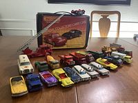 Photo showing all 24 Matchbox diecast vehicles arranged in front of the official collectors' carry case. Vehicles include fire truck with extendable ladder, ambulances, trucks, and vintage cars.