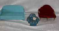 Front view of three doll house furniture pieces: blue wooden loveseat, blue ceramic armchair, red upholstered wooden settee.