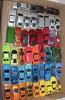 Top view of diecast cars in various colors including silver, white, green, red, blue, and yellow neatly arranged in rows inside a box.