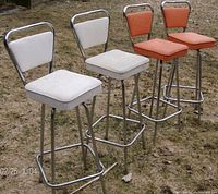 Four retro barstools with two red vinyl and two white vinyl upholstered seats and backs, all on aluminum frames, shown outdoors on grass.