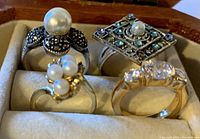 Front view of four rings placed in a soft jewelry box, showing pearl, crystals, and clear stones on varied bands.