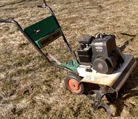 Side angle view of the rototiller showing metal frame, engine, and tilling blades.