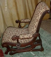 Side angle showing carved walnut armrest, upholstery pattern, and rocking base