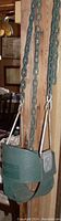 Green high back full bucket infant swing seat attached to heavy-duty coated iron chains and metal hooks, hanging indoors near a wooden post.