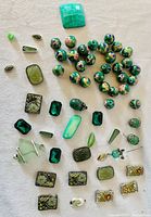 Top-down photo showing large assortment of green jewelry making supplies including various beads, crystals, and stones arranged on a flat surface.