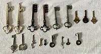 Full view of 20 skeleton key charms arranged on a white cloth background showing variety in sizes and styles.