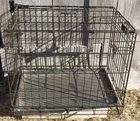 View of the MidWest iCrate folding metal dog crate showing the overall structure, black metal frame with plastic leak-proof tray and floor protecting feet.