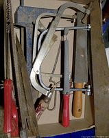 Top view of assorted tools containing hand saws, hacksaw, files, and caulking tool in a cardboard box