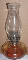 Vintage oil lamp with amber glass base, clear glass beaded top hurricane shade, metal burner, and wick adjustment knob.