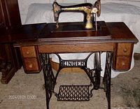 Front view of vintage Singer treadle sewing machine on oak cabinet with drawers and metal pedal stand.