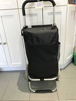 Black shopping buggy cart with fabric cover and thick padded handle shown standing upright against kitchen cabinets.