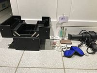 Closed view of black fold-out makeup case, blue eye mask, blow dryer, small bottles, compact powder, and makeup accessories