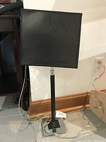 Full side view of black table lamp with square black lampshade and chrome base, cord visible on floor.