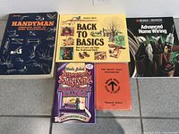 Five books arranged on tiles: Handyman guide, Back to Basics, Black & Decker wiring, Bathroom Reader, and Bruce Trail Guidebook.