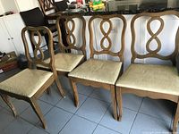 Four vintage wooden dining chairs with ornate double-loop backrests and upholstered beige seats arranged in a kitchen area.