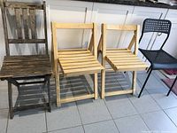 Front view of two light wood folding chairs, dark wood folding chair, and black plastic chair on tile floor
