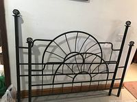 Front view of black metal queen size headboard with sunburst metal design and decorative open sphere finials on top of posts.