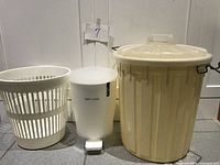 Full view of three plastic bins including the large cream-colored bin with lid and locking handles, a medium white pedal bin labeled 'KEEP CLEAN', and a white plastic laundry basket with slots.