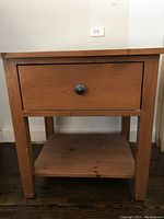 Front view of wooden side table featuring a single drawer with round knob and lower shelf.