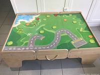 Full front view of the wooden toy train table with its road play mat surface and storage drawers.