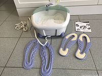 Photo showing WaterPik Retreat pedicure foot spa basin on floor with power cord and included purple detachable aromatherapy pads and replacement insoles, plus instruction manual beside unit.