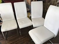 Four white leather chairs with chrome cantilever frames arranged in a row on wooden floor. View from front and slightly above showing seat and backrest condition.