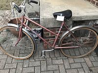 Full side view of the reddish brown step-through frame bicycle showing tires, pedals, seat and handlebar.