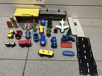 Photo of wooden magnetic train set including trains, airplane, station, vehicles, figures, and accessories laid out on tiled floor.