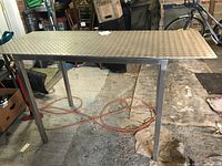Full side view of the work table showing diamond plate aluminum top and stainless steel legs in an industrial environment.