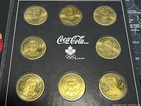 Photo of 8 gold-colored hockey player medallions arranged on black backing with Coca Cola and Olympic logos.